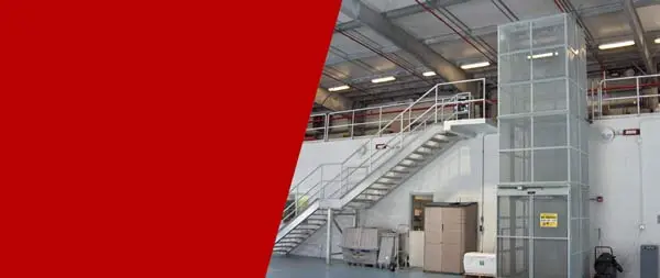 KABTech's Vertical Material Lift Next To A Set of Stairs in a Warehouse